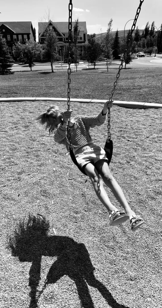 Shadows by Kay Lindon. A girl swings with her hair flying. Her shadow displays a more luxurious set of locks.